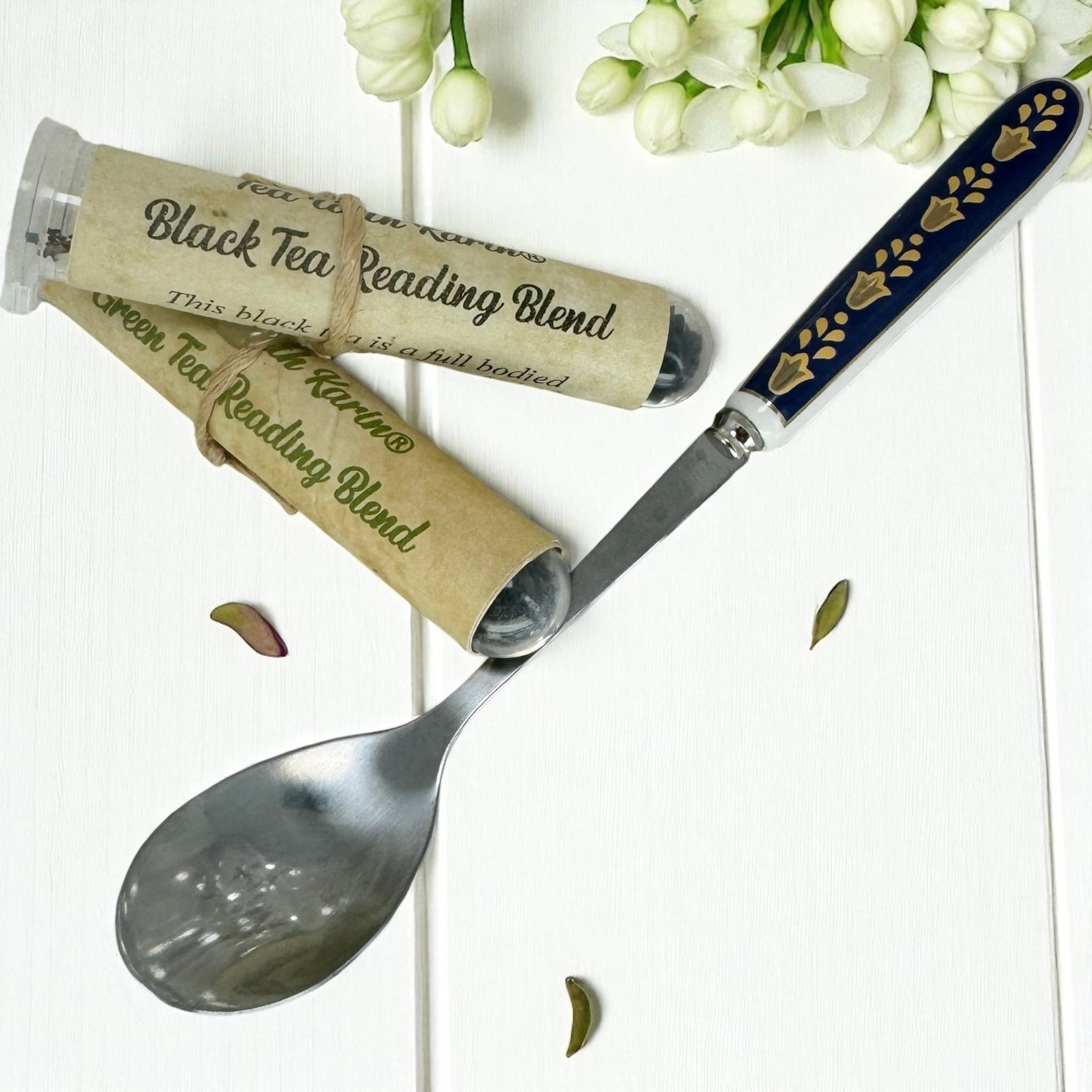 Spoon with decorative handle, tea packaging, and white flowers on a light background