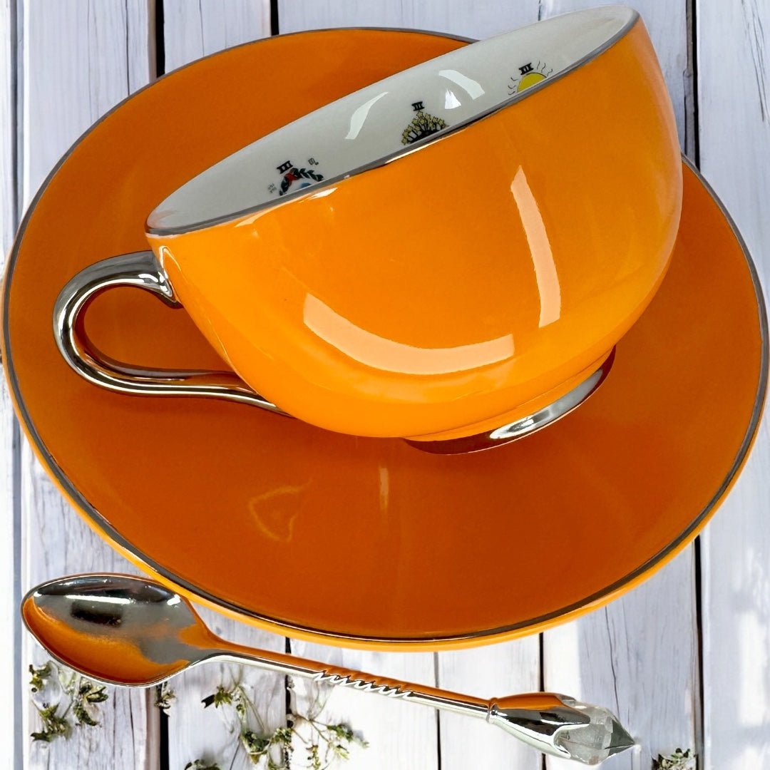 Left side view of the bright orange teacup tilted on the matching saucer, showcasing the cup's smooth finish and silver accents.