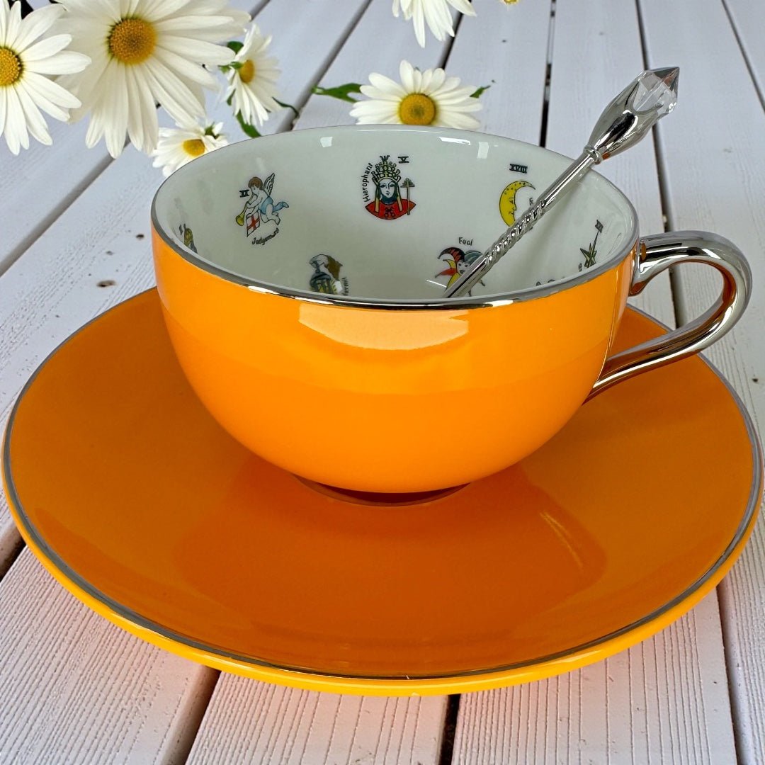 Orange teacup with a reflective silver handle resting on its saucer, showing the white interior with internal imagery visible.