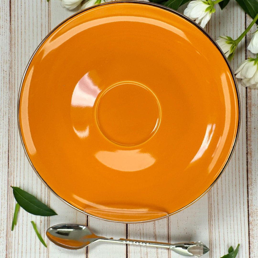 Overhead view of a solid orange saucer with a silver rim, featuring a crystal-tipped silver teaspoon below it.