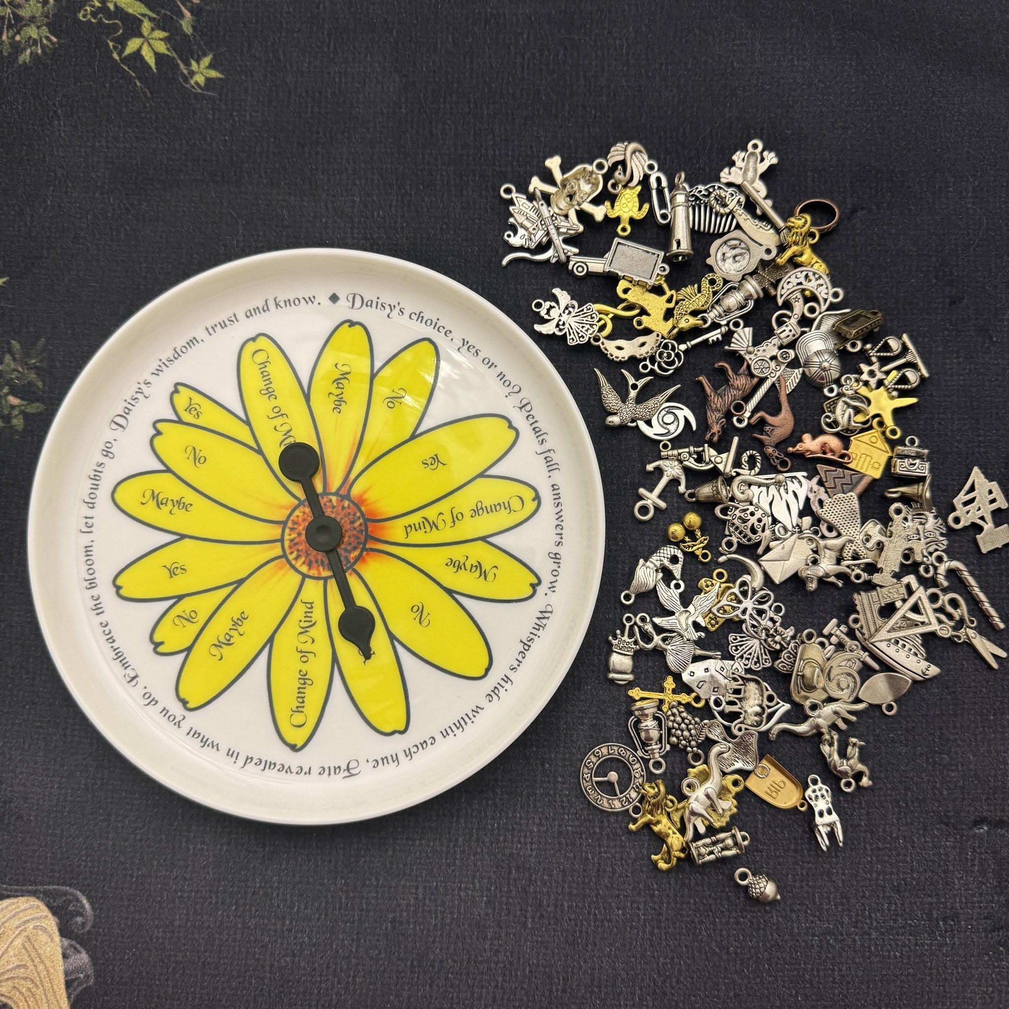 Pick a Daisy spinner plate beside a pile of silver and gold divination charms for charm casting