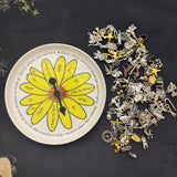 Pick a Daisy spinner plate beside a pile of silver and gold divination charms for charm casting