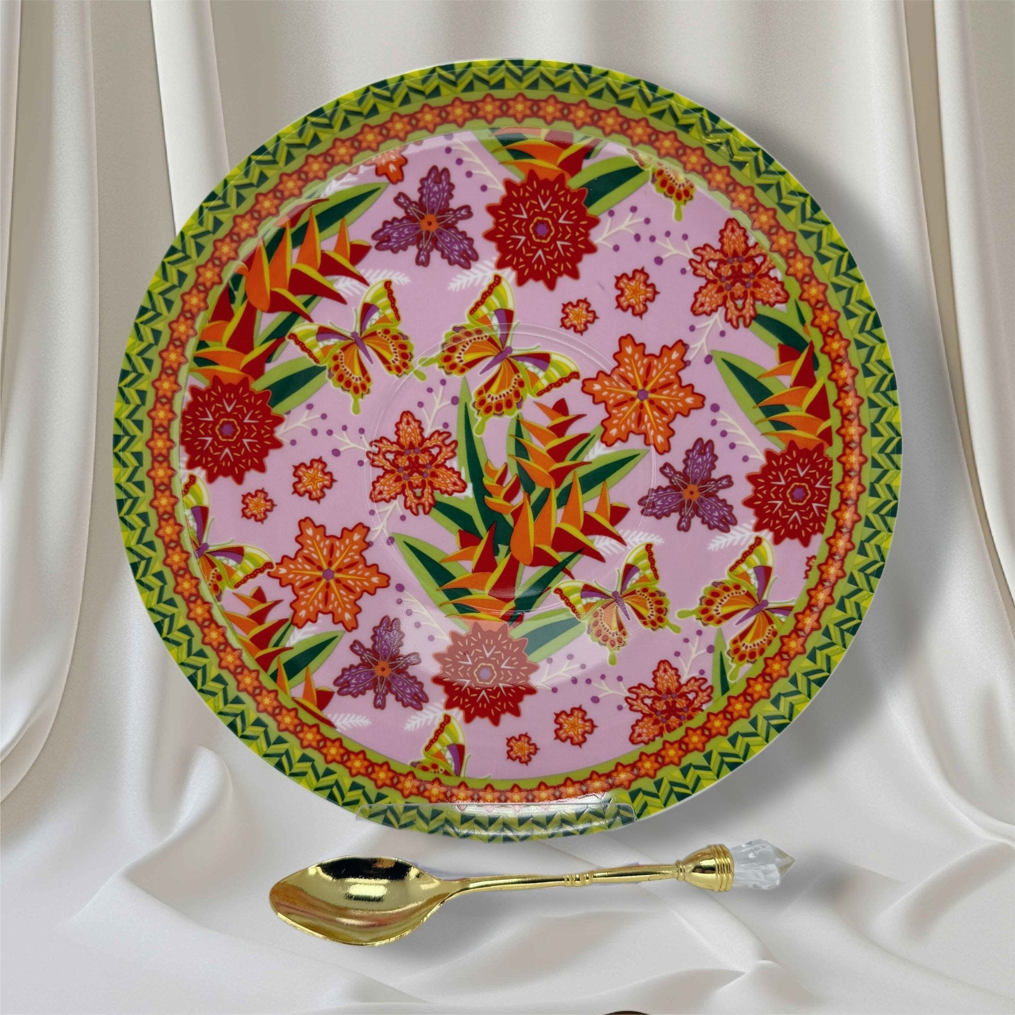 Pink saucer with vivid orange and green floral, butterfly pattern and a crystal-handled gold teaspoon