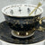 Black tarot-themed teacup and saucer set with mystical tarot symbols inside, accompanied by a symbol guidebook and a gold teaspoon, ideal for daily tea leaf reading and divination