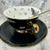A detailed view of the Death Moth Teacup showing the elegant moth and moon illustrations, with gold embellishments on a dark background, emphasizing its luxurious and gothic aesthetic.
