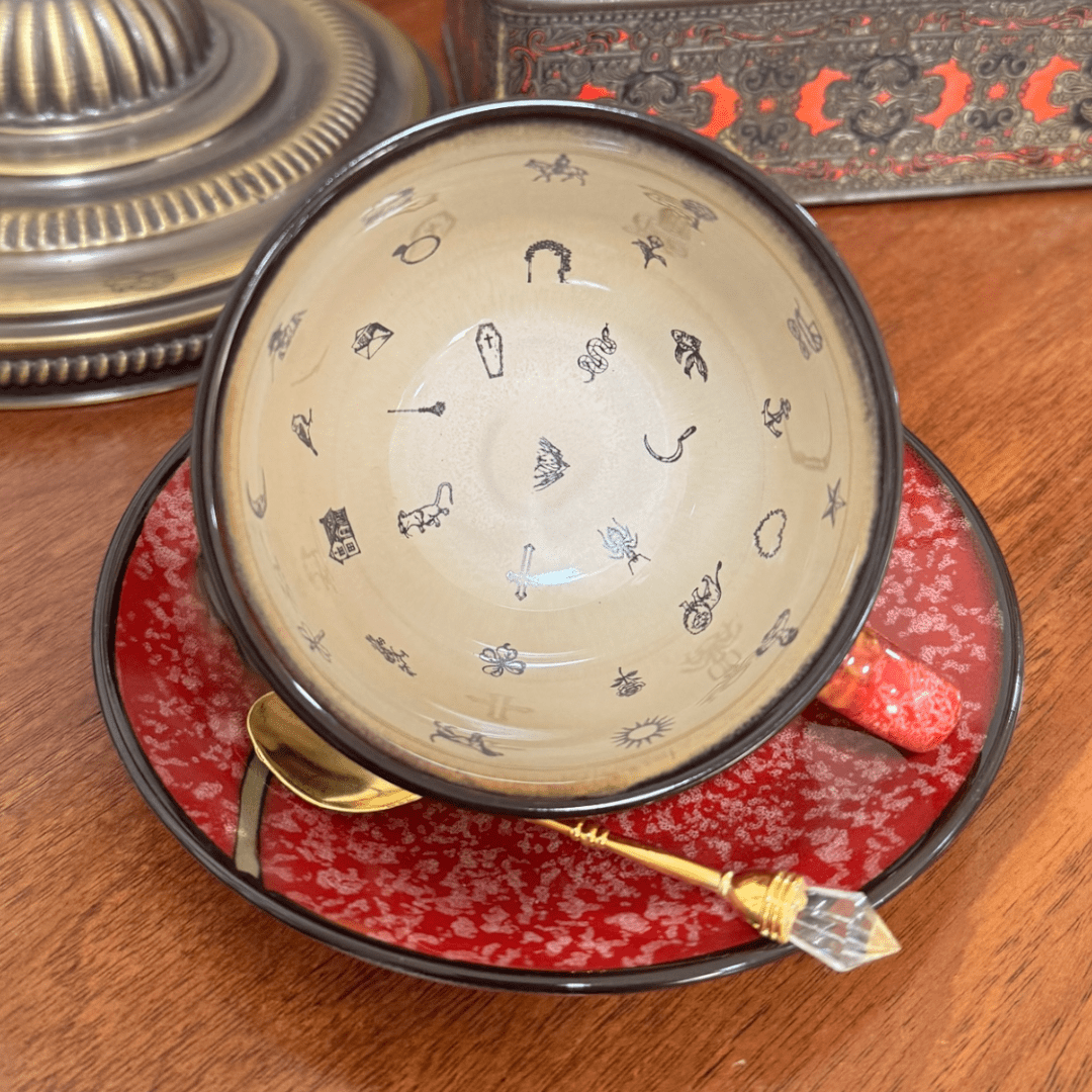 Decorative bowl with Lenormand symbols on a red plate with a gold spoon, all on a wooden surface.