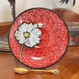 Decorative plate with a white flower design on a red speckled background, accompanied by a gold spoon.
