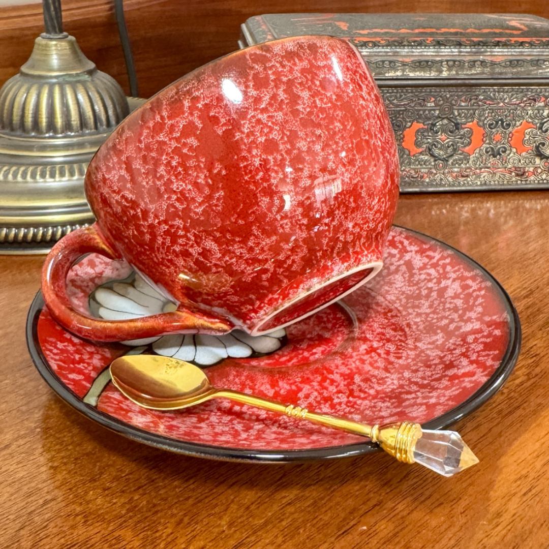 Red ceramic cup and saucer with a gold spoon on a wooden surface