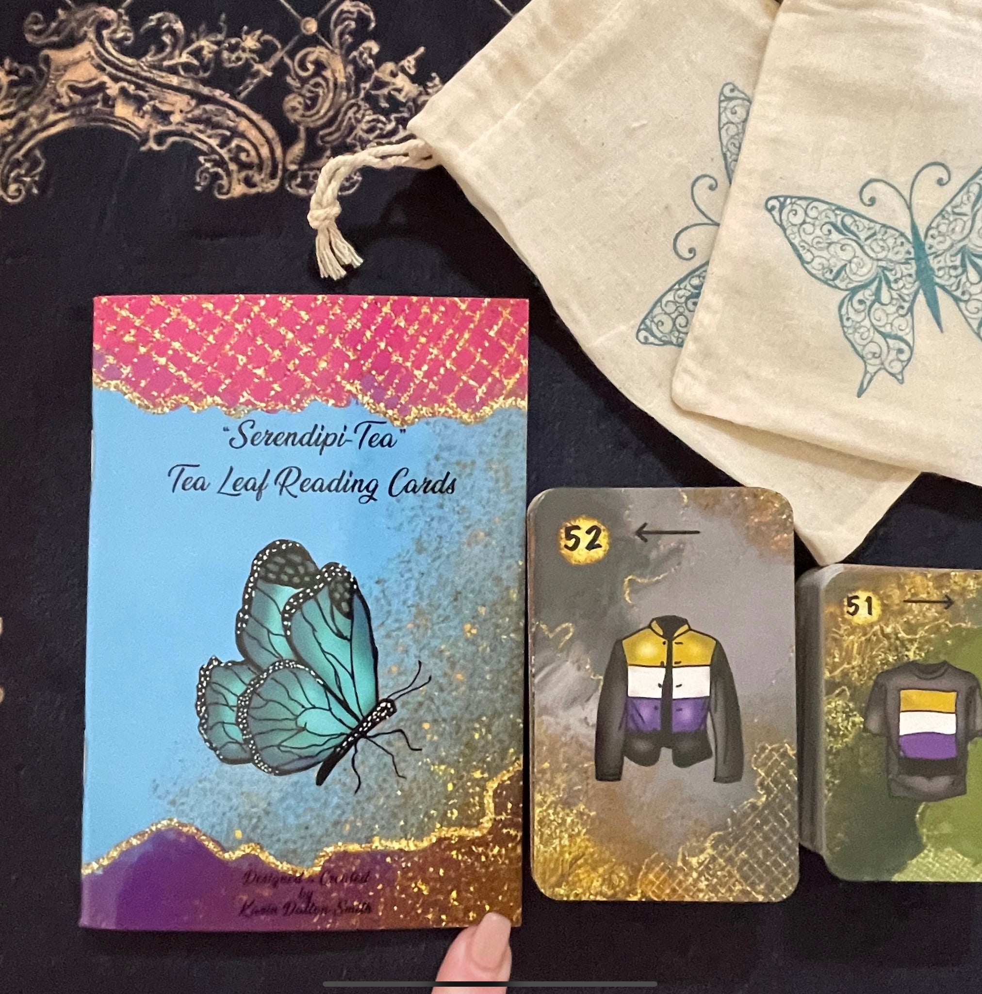 A beautiful 52-card tea leaf reading deck with vibrant watercolor-style illustrations, displayed alongside a soft cotton drawstring bag and a small gold teaspoon. 