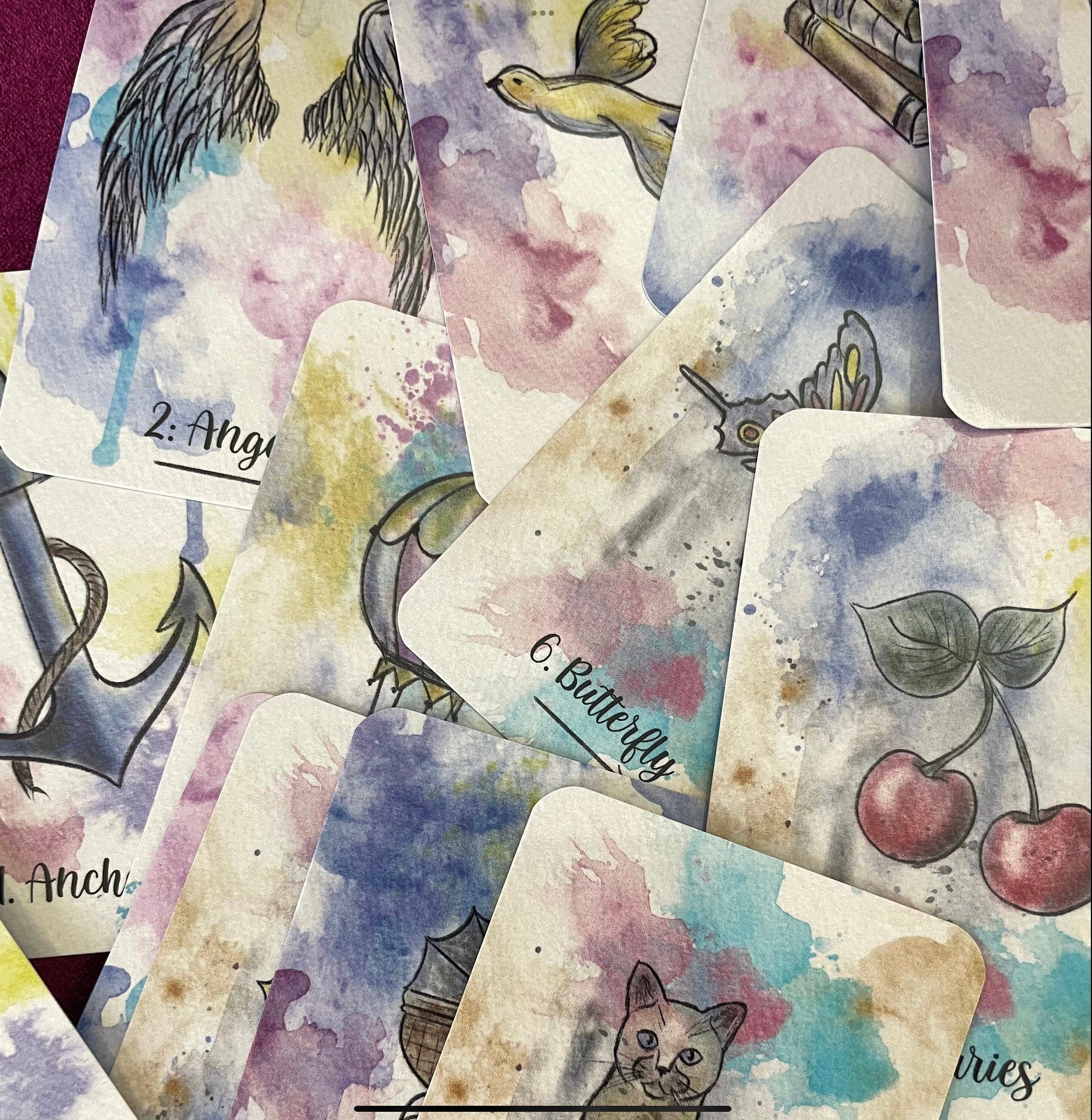 A soft watercolor deck titled “Sereni-Tea” with pen outline images, displayed in a spread showing vibrant, detailed cards.  