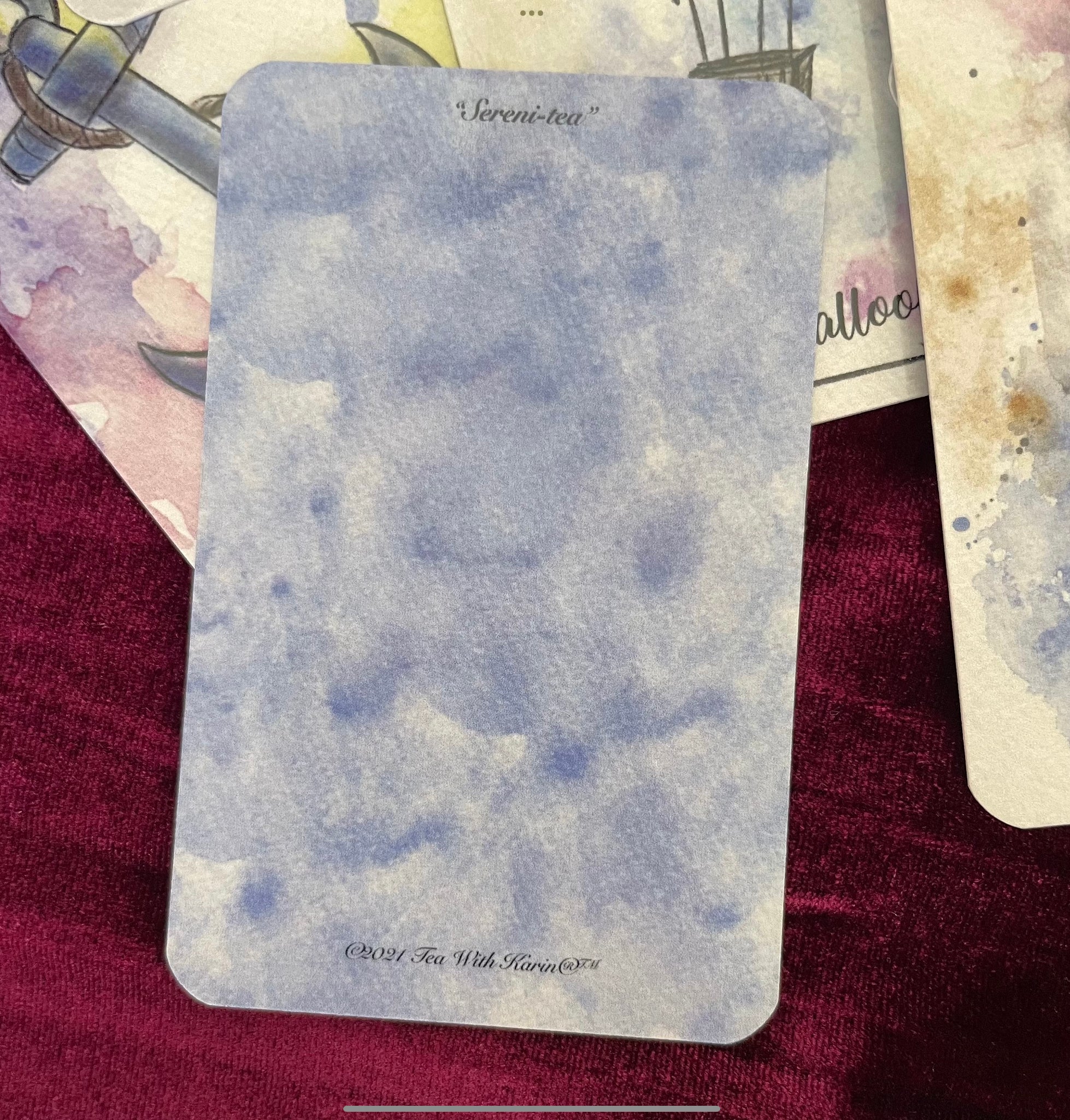 A soft watercolor deck titled “Sereni-Tea” with pen outline images, displayed in a spread showing vibrant, detailed cards.  