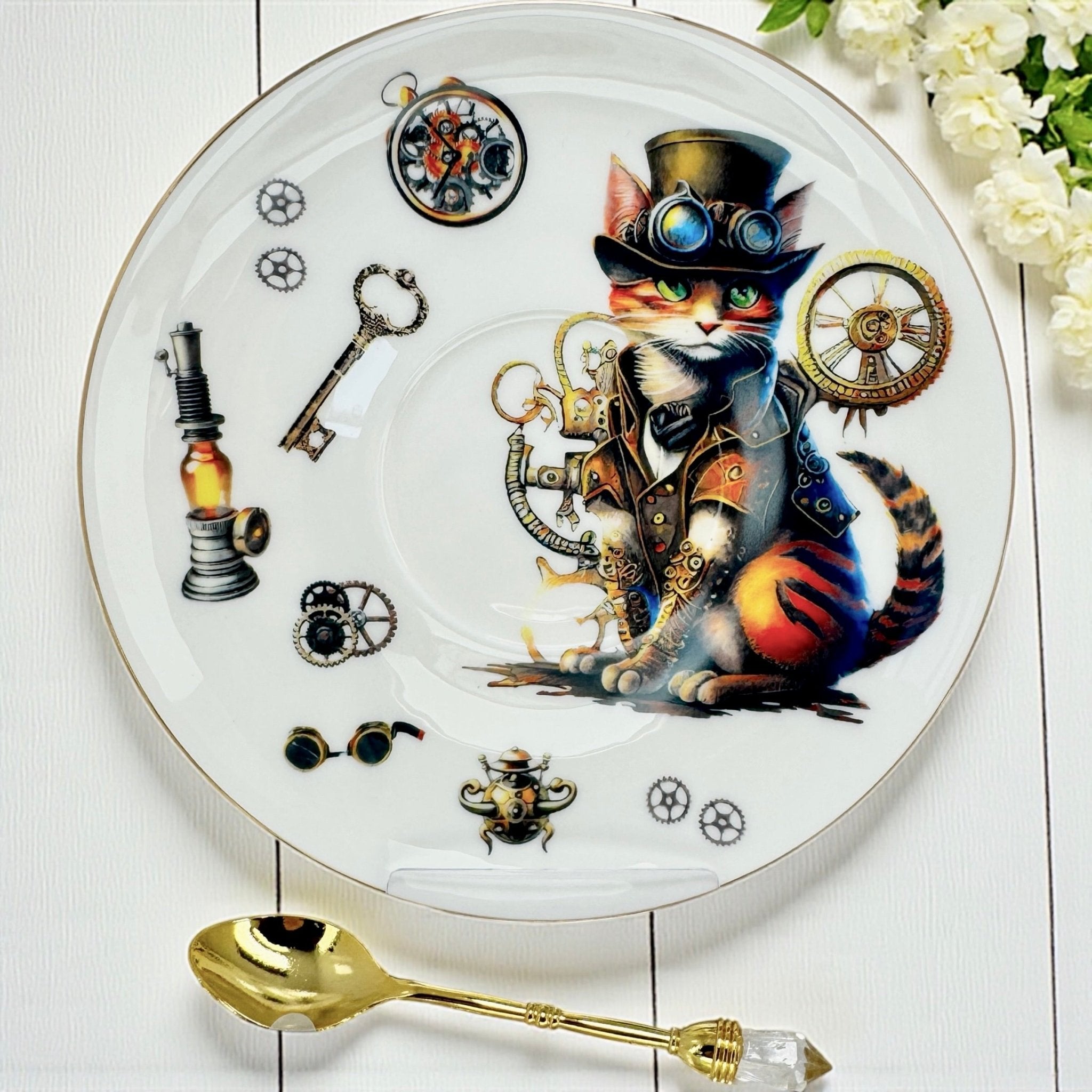 A teacup and saucer set featuring a steampunk-style cat, along with a gold spoon with a clear crystal handle and two small tubes of tea.