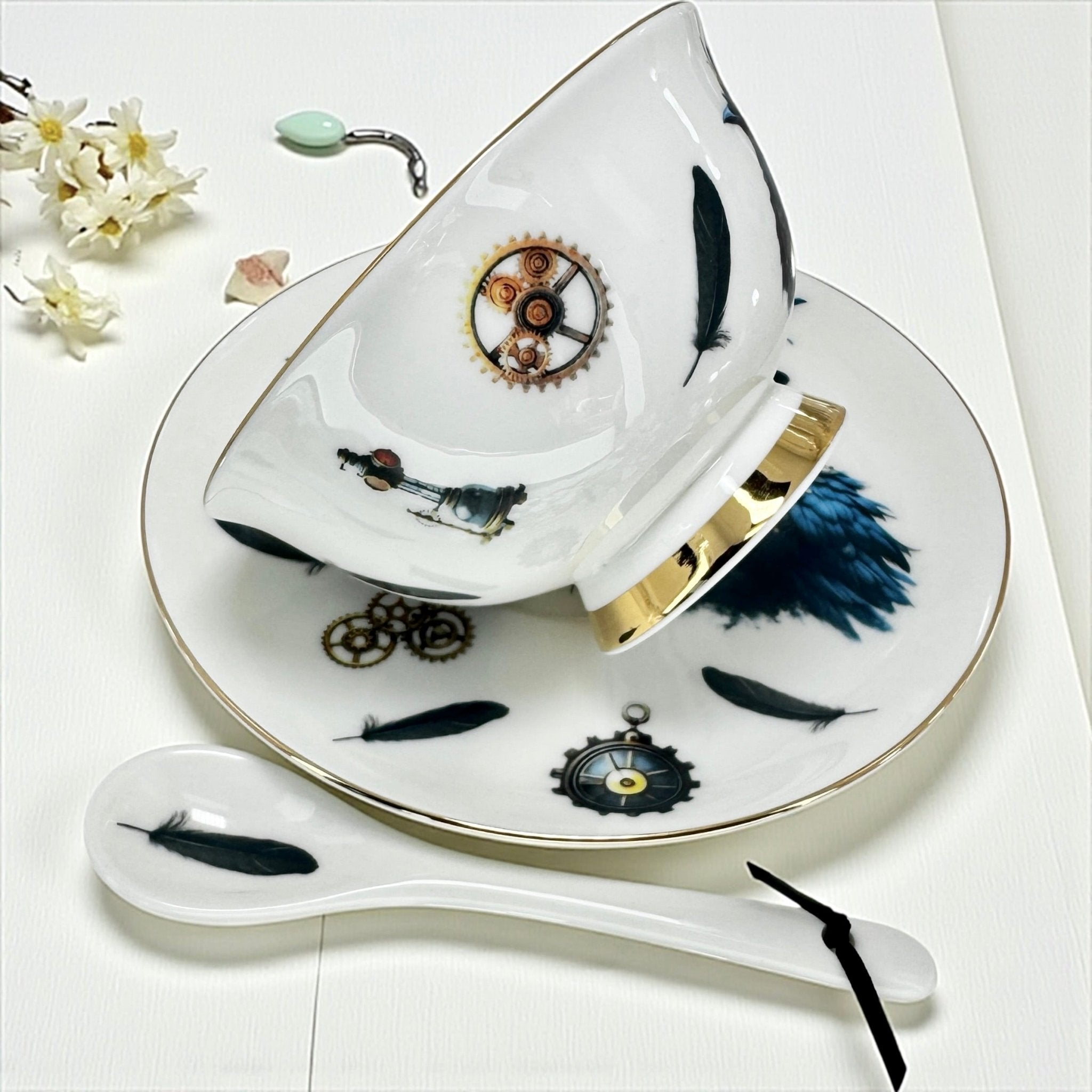 Side view of the teacup and saucer set, highlighting the gold accents and detailed steampunk crow motif.  