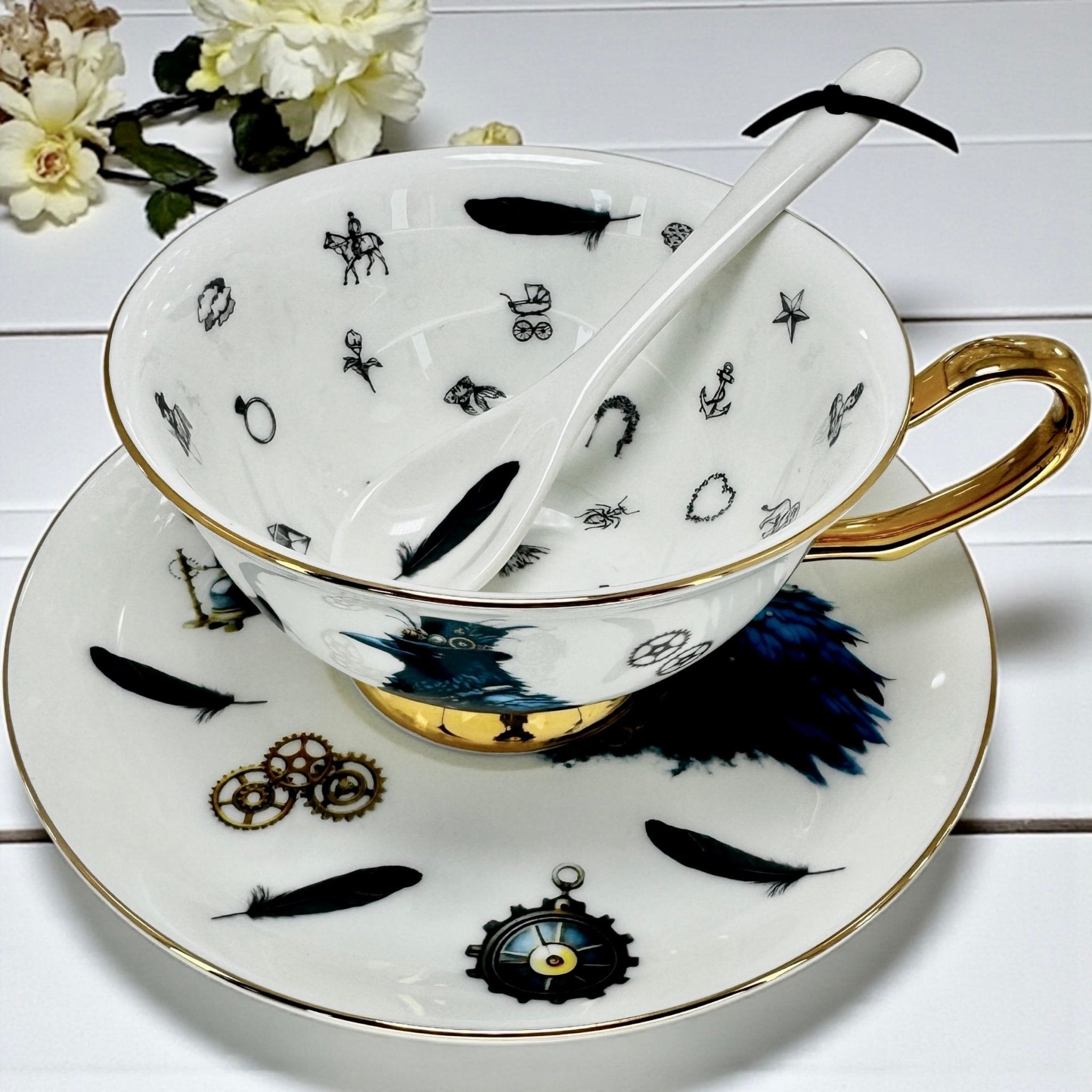 Angled view of the teacup on the saucer, displaying the crow design, gold trim, and decorative motifs, with flowers in the background.