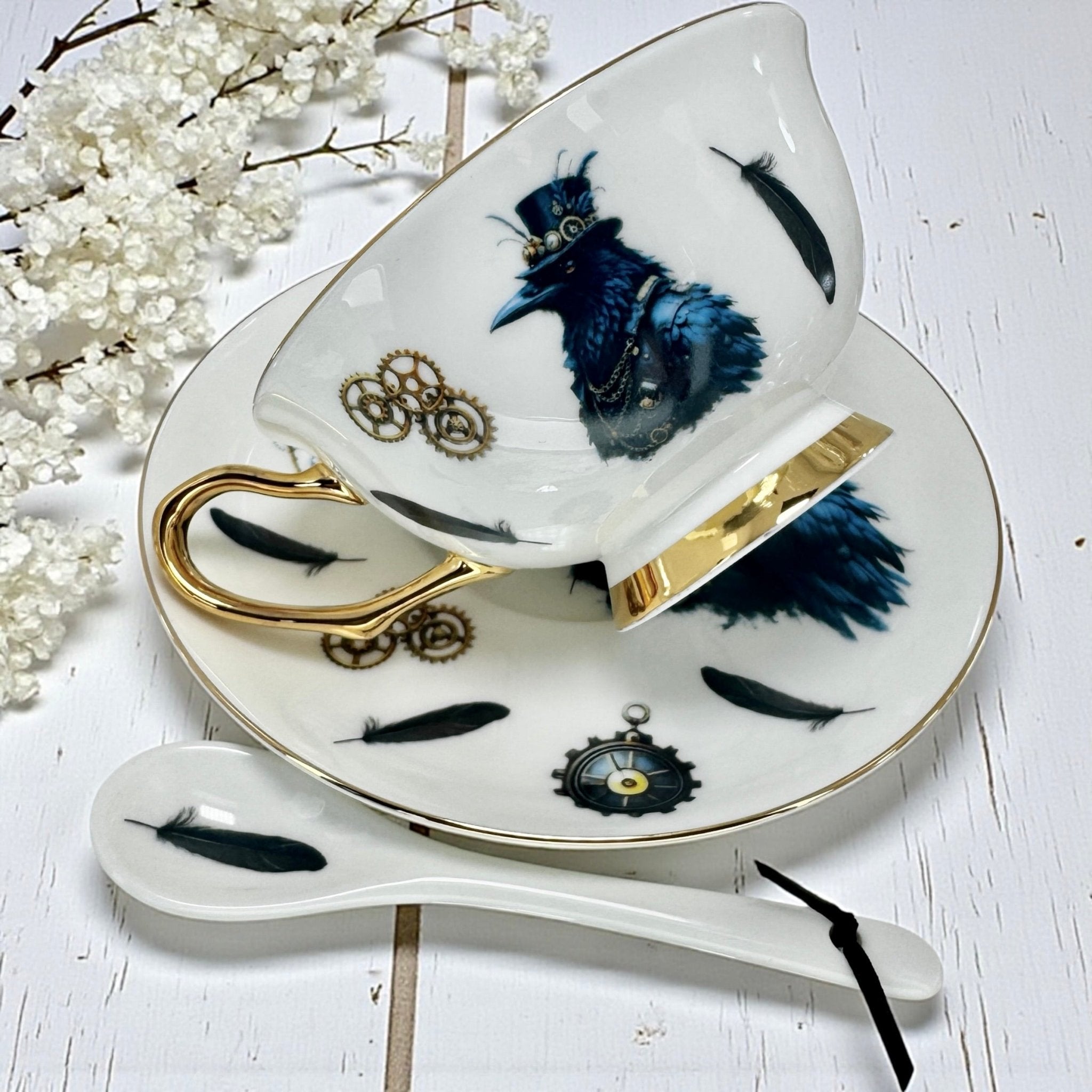 Elegant teacup with steampunk crow design, gold trim, and matching saucer, featuring gears, feathers, and clockwork illustrations