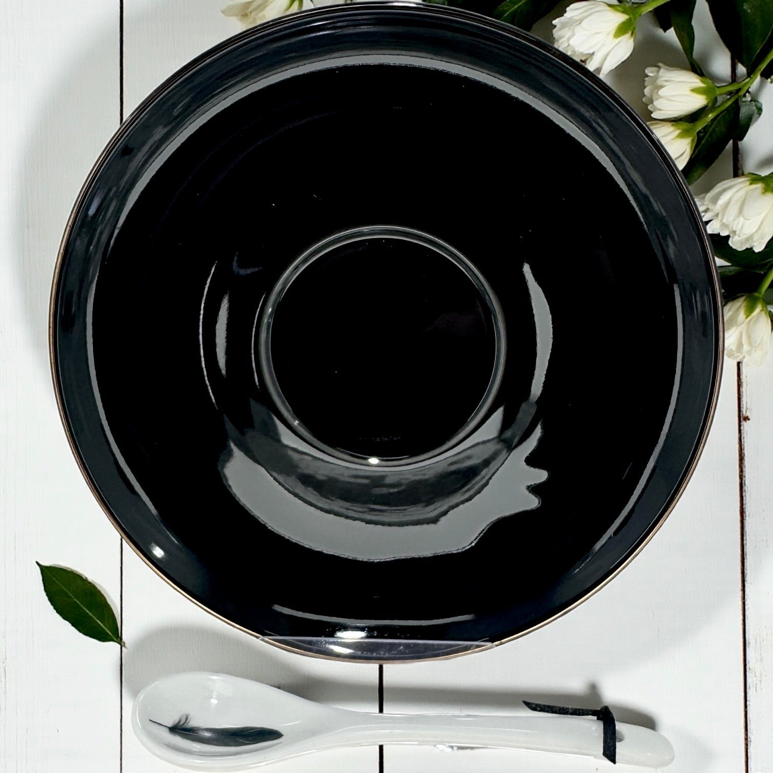 Black ceramic plate on a white wooden surface with a white spoon and flowers.