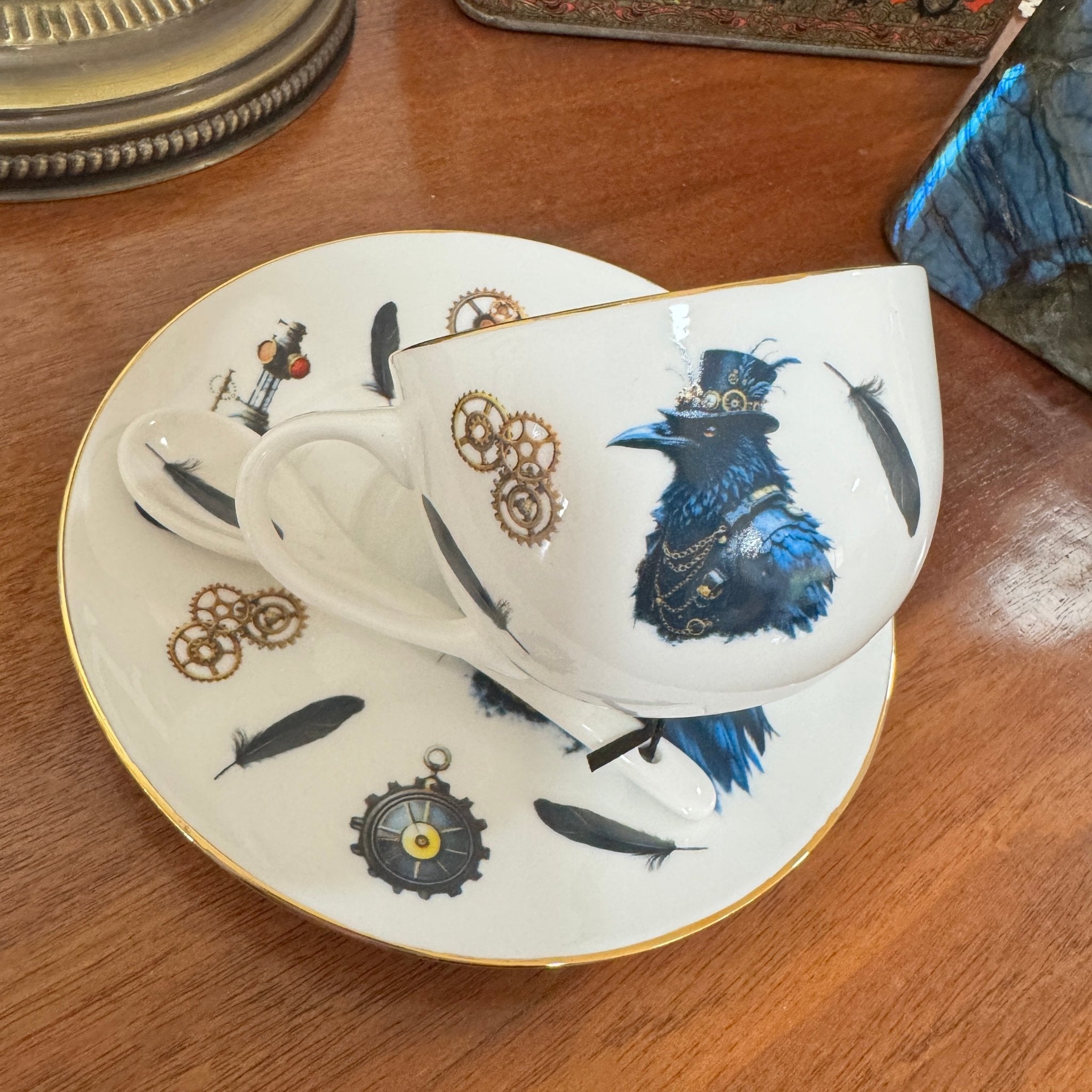 Teacup and saucer with decorative s teampunk crow design on a wooden surface