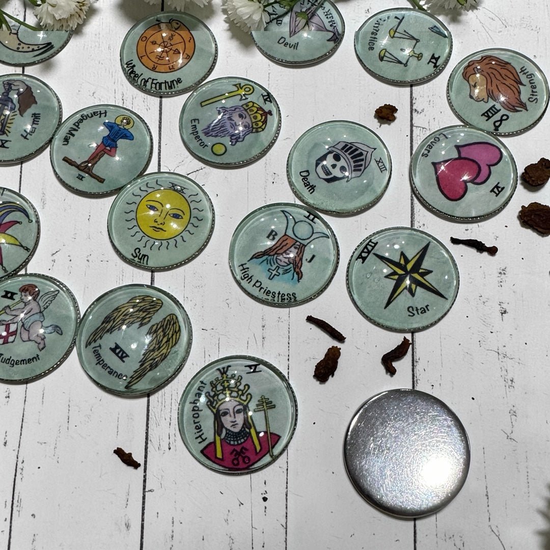 Tarot charm casting coins spread on a wooden surface showing the smooth polished metal backing plate alongside glass-topped coins with illustrated Major Arcana designs