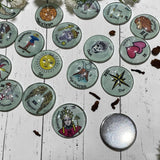Tarot charm casting coins spread on a wooden surface showing the smooth polished metal backing plate alongside glass-topped coins with illustrated Major Arcana designs