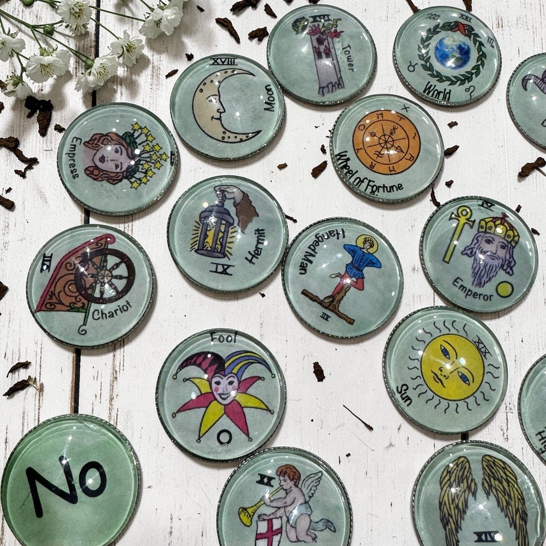 Close-up view of Major Arcana tarot casting coins showing detailed hand-drawn artwork beneath clear glass dome tops on polished metal bases