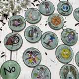 Close-up view of Major Arcana tarot casting coins showing detailed hand-drawn artwork beneath clear glass dome tops on polished metal bases