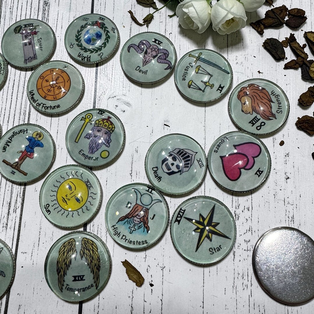 Major Arcana tarot charm coins scattered on dark wooden surface displaying glass dome fronts with colourful illustrations and one flipped coin revealing the smooth silver metal backing