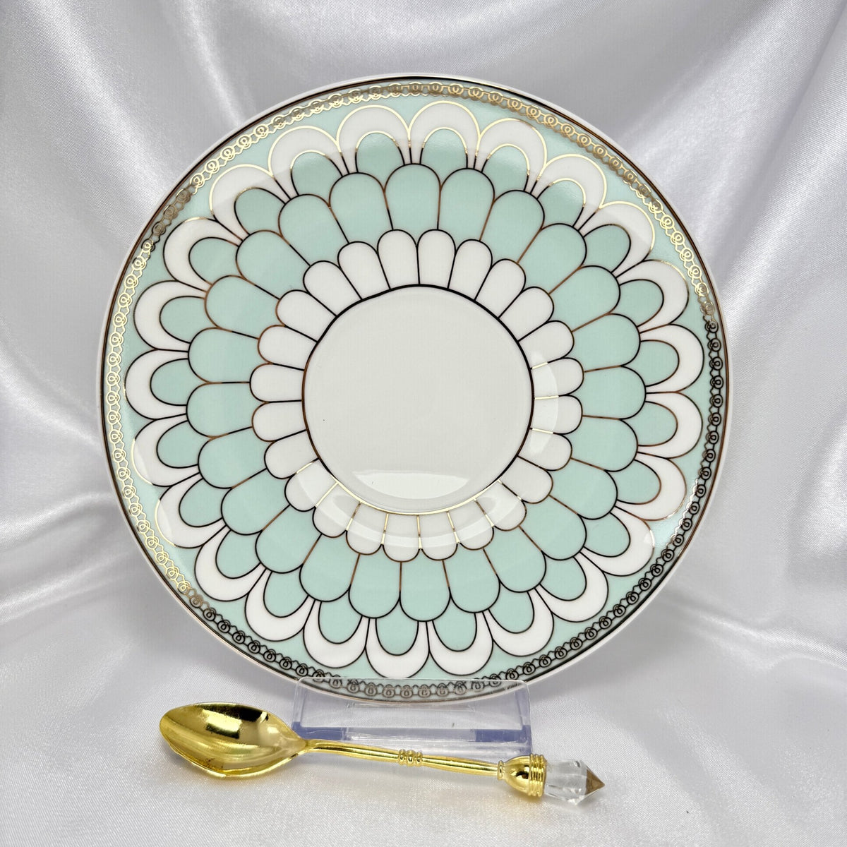 Porcelain saucer with mint green and white scalloped pattern, gold trim, displayed with an ornate gold teaspoon.