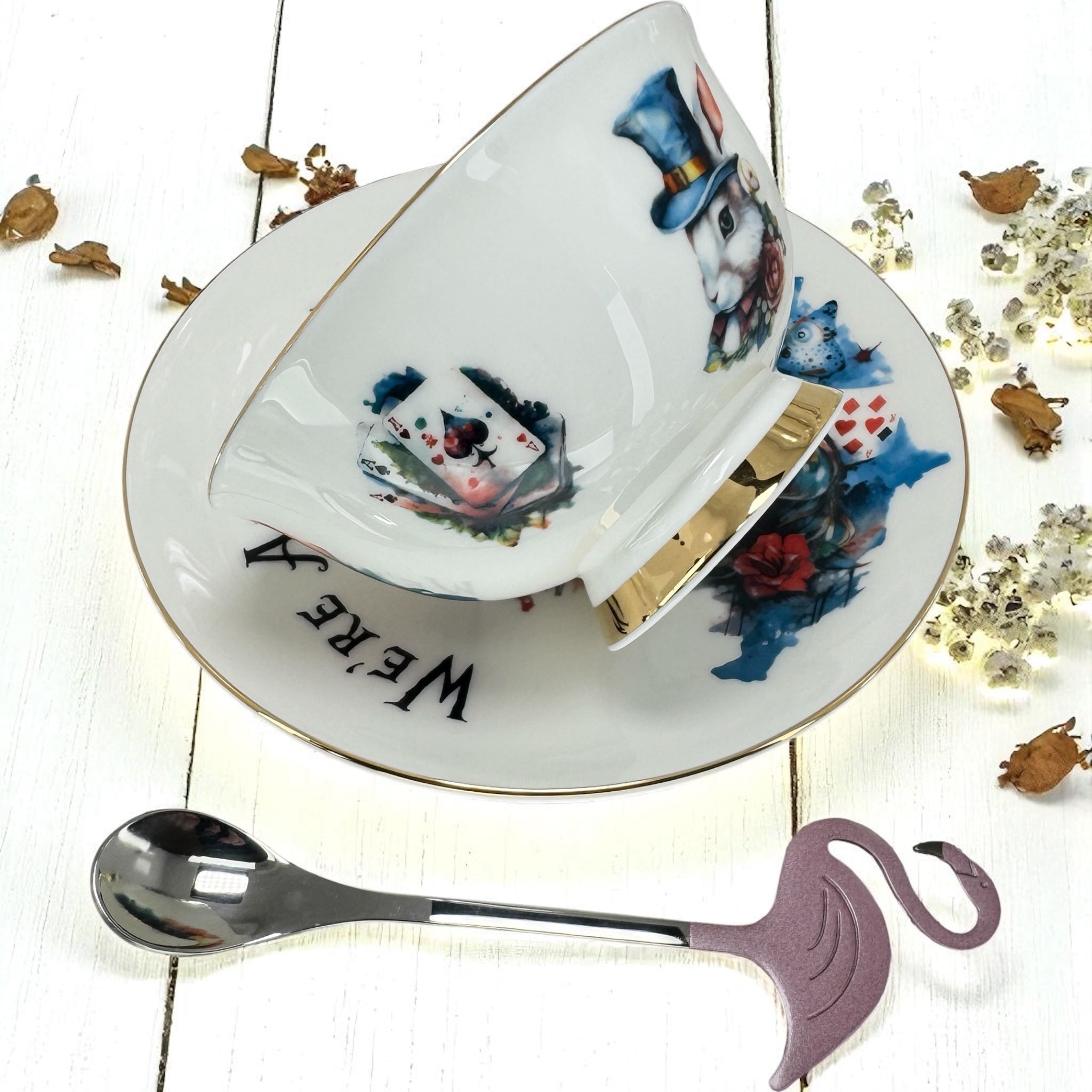 Tea cup and saucer with decorative design on a white wooden surface with a spoon and flamingo-shaped spoon rest.
