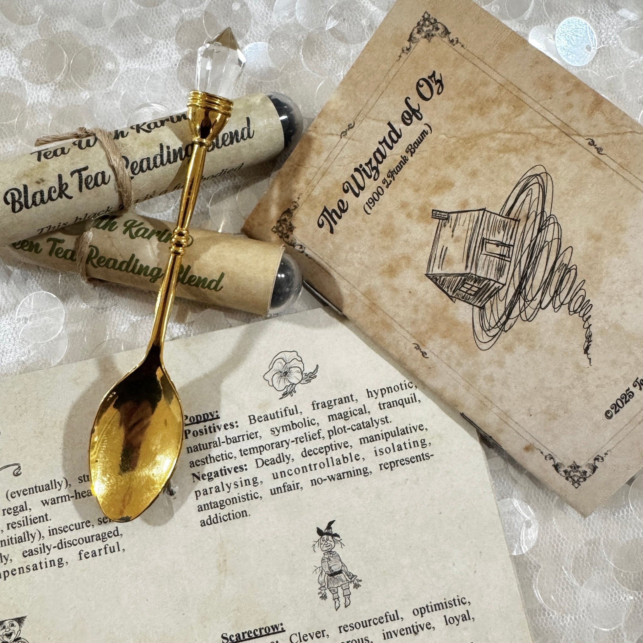 Gold spoon on a piece of paper with 'The Wizard of Oz' book and tea packages in the background.