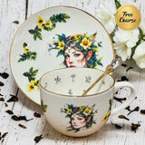 Woodland Fairy Elf Tea Reading Set — gold tasseography teacup and saucer with elf portrait and yellow floral design with crystal spoon on white wooden surface | Tea Leaf Reader