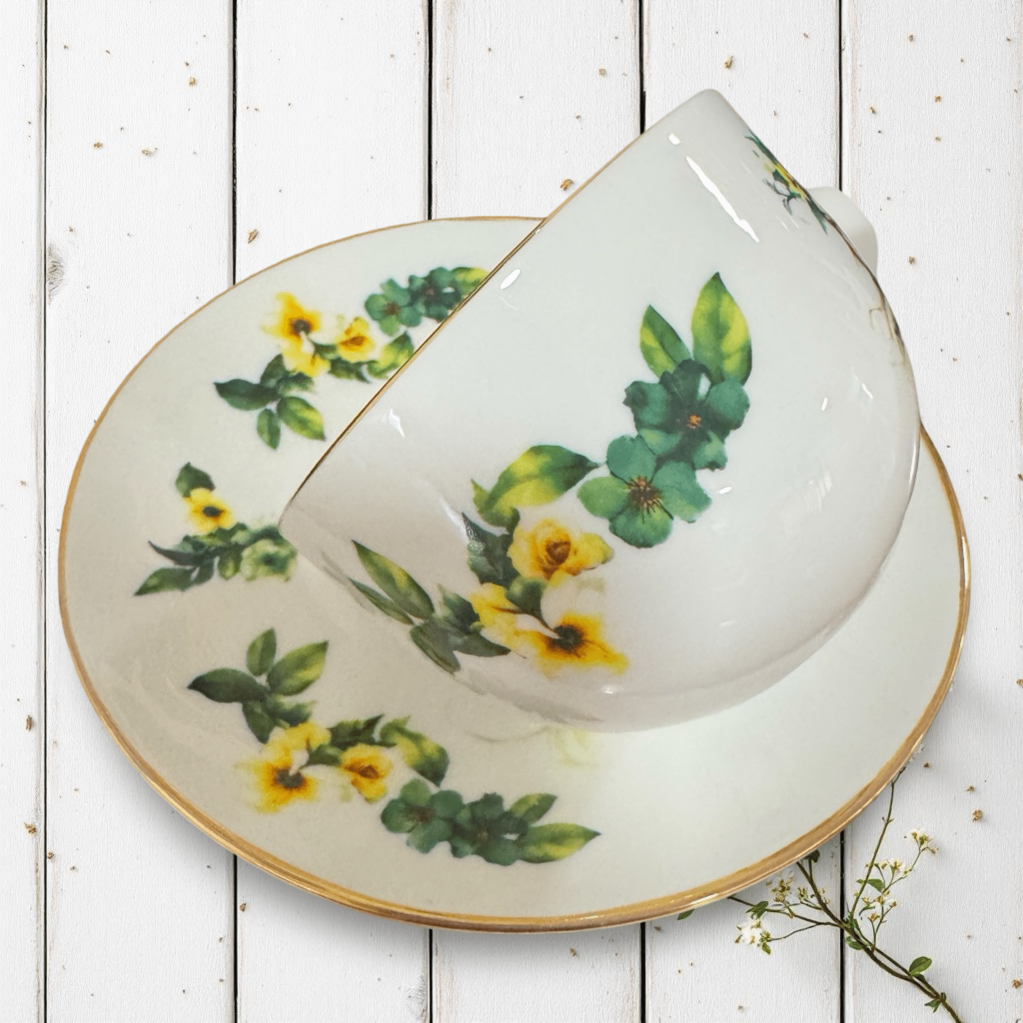 Woodland Fairy Elf Tea Reading Set — tilted view of gold tasseography teacup on saucer showing yellow botanical floral design on white wooden surface | Tea Leaf Reader