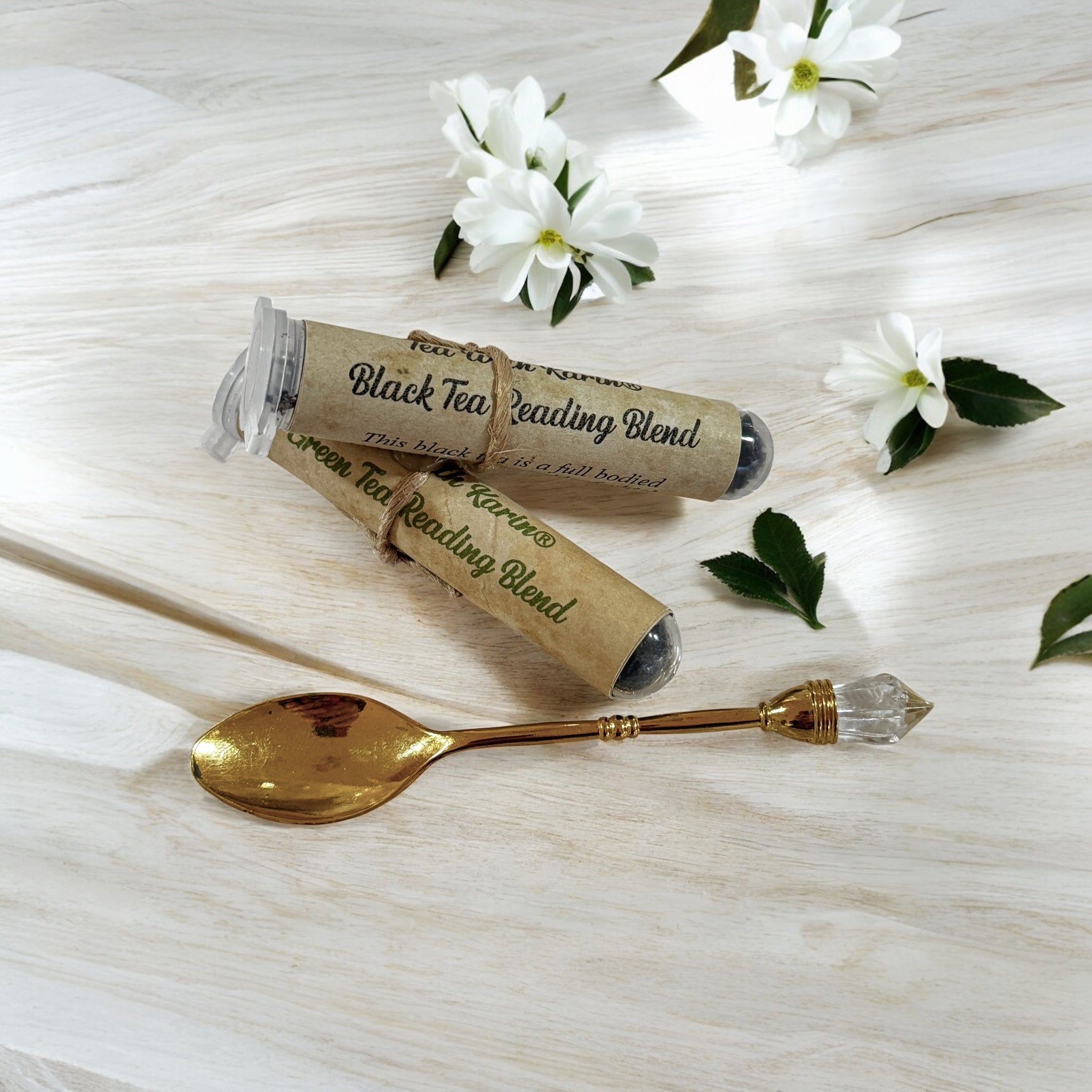 Tea packaging with a decorative spoon on a light wooden surface with white flowers.